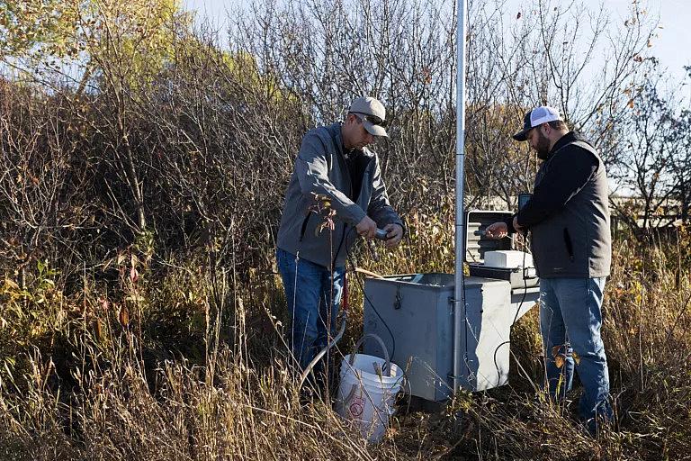 Water resources technicians Josh Schnitzler and Connor Baldwin, who both work for the Lower Elkhorn Resources District in Norfolk, prepare to test the water in a monitoring well near the north fork of the Elkhorn River. They were working at a nested location of three wells that run from shallow to more deep and are used to monitor groundwater for nitrates and other substances like solids and sulfates. The wells are located about 10 miles northwest of Elkhorn. Photo by Ryan Soderlin for the Flatwater Free Press