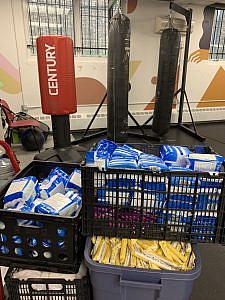 Crates of menstrual pads and tampons stored near punching bags and other boxing equipment before pantry distribution begins.
