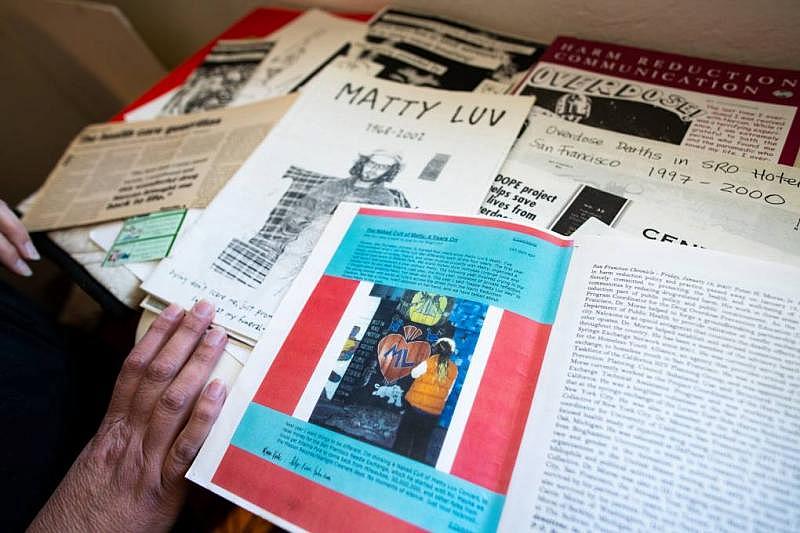 Rachel McLean looks through her archive of flyers, zines, educational information, and research on harm reduction at her home on March 10, 2022. A photo of friend and colleague Pete Morse can be seen, as can a zine about Matty Luv, singer of the San Francisco punk band Hickey, who passed away from a heroin overdose in 2002. (Beth LaBerge/KQED)