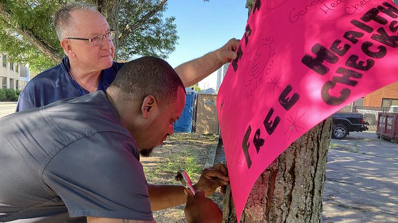 Driver John Hayes (left) helps Nurse Neville Johnson post a sign outside CODAC's mobile clinic. LYNN ARDITI/THE PUBLIC'S RADIO