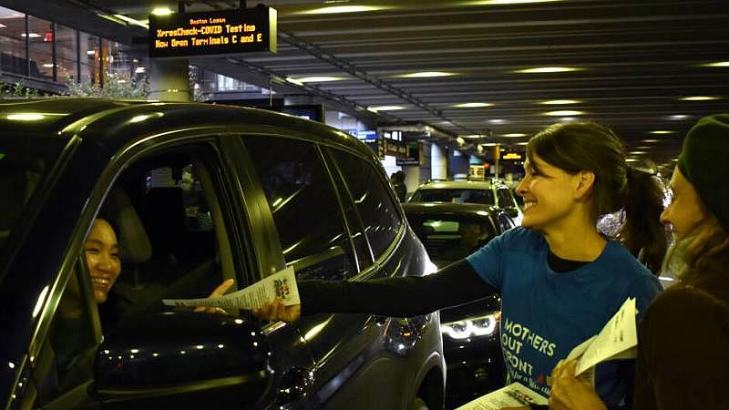 Sonja Tengblad hands an information sheet to a driver idling outside of Logan Airport's Terminal B