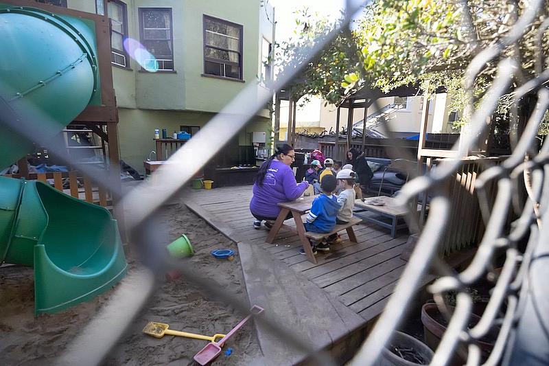 Isabel Daniels (left) and Sophia Lam (right) run through card games with children at Baby Steps, a family child care provider in San Francisco, in November.(Paul Kuroda / For The San Diego Union-Tribune)