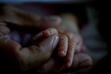 Bruce McQuakay holds the fingers of his daughter and first child, Mishiike Meteh McQuakay KingBird, six days after her birth.