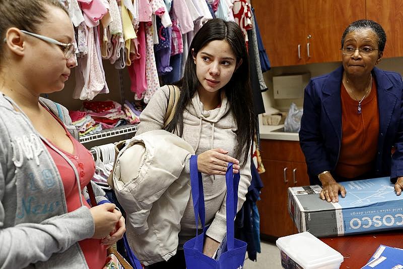 Stephanie Ulloa, left, and Paola Ramirez, with facilitator Jean Lawrence, right, pick out clothes for their babies after a Stork's Nest prenatal class in Converse on Dec. 15. Ramirez received a stroller for attending all eight classes.