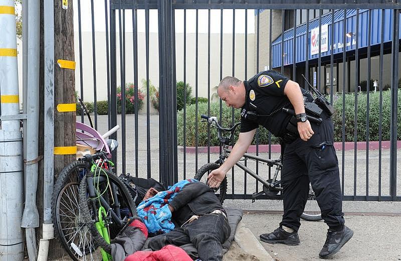 Jacob Jundef, a homeless liaison officer for the Oxnard Police Department, wakes up a homeless man from a fence along a business where he is not allowed.