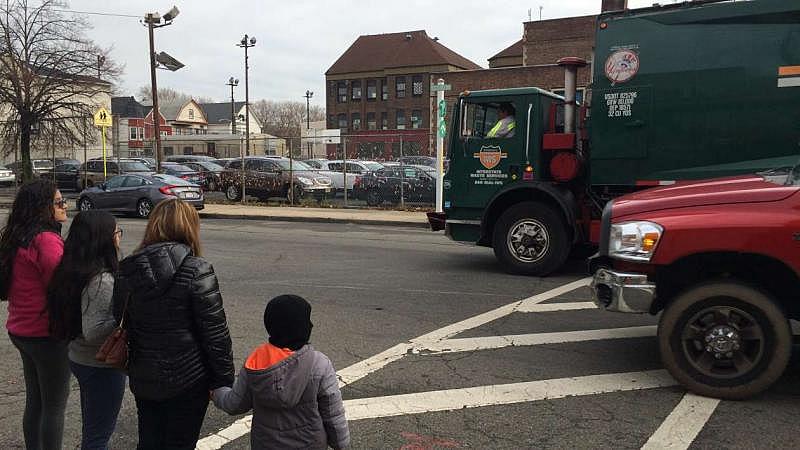 	  Trucks rumble along the road outside Hawkins Street School in Newark, New Jersey, as a family waits to cross.  Jamie Smith Hopkins / The Center for Public Integrity 