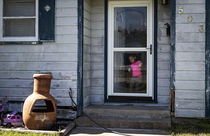 Tiana Crane, 2, draws on a glass storm door with a marker while her mother isn’t looking. The front door of her home is left open to let light into the living room in August. [Photo by Angela Piazza]