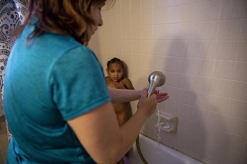 Tiana cowers from her mother in the corner of the shower because she does not like having her hair washed. Even though Angelica is ill from intensively cleaning her home the day prior, she bathes her two girls and applies prescription ointments to their skin. [Photo by Angela Piazza]