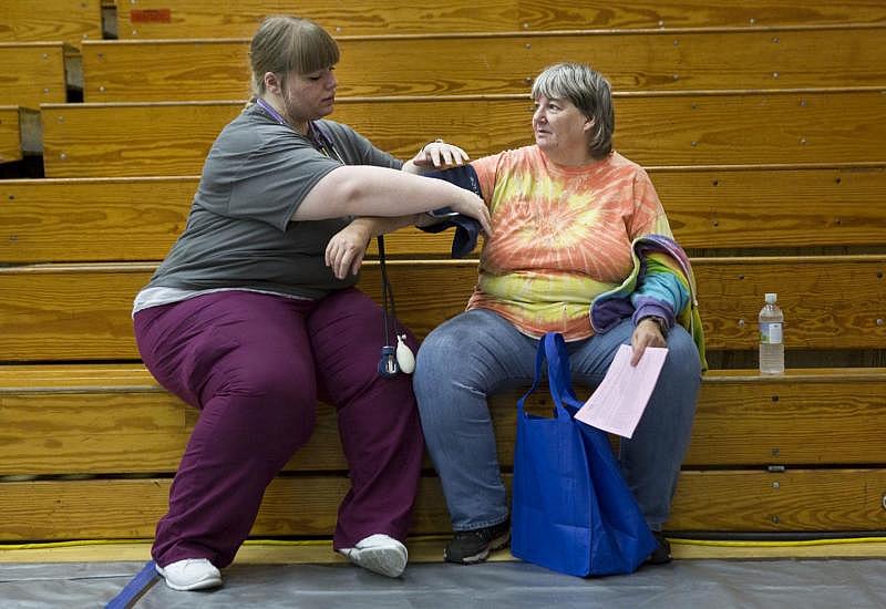 Nursing student volunteer Chelsey Lewis of Jonesville retakes a blood pressure reading for Cheryl Howe, who lives on a farm near Jonesville. Howe was waiting to have teeth pulled but was not permitted to enter the dental clinic until her pressure fell. She was diagnosed with hypertension a few months earlier when she went to an emergency room for abnormal bleeding and cramping, but she could not afford to go to a primary care clinic to get a prescription.