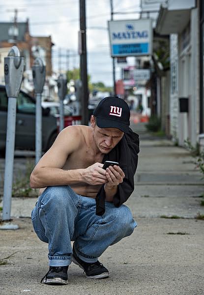Travis Litts crouches down on the sidewalk along East Ridge Street in Lansford to answer text messages. (Photo Credit: Rick Kintzel/The Morning Call) Travis Litts crouches down on the sidewalk along East Ridge Street in Lansford to answer text messages. Rick Kintzel / The Morning Call