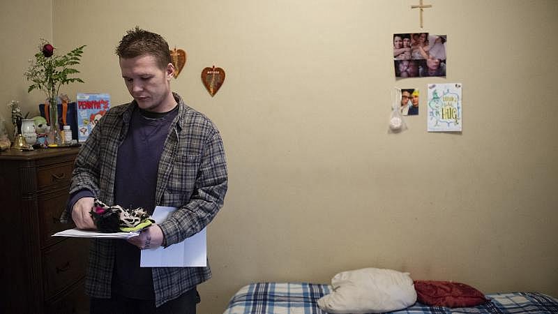 Travis Litts stands in his bedroom at his Lansford apartment while holding clothing and medical paperwork. Rick Kintzel / The Morning Call