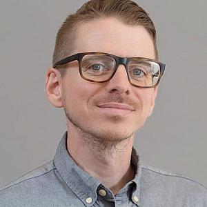 Person in gray shirt and glasses with a black frame
