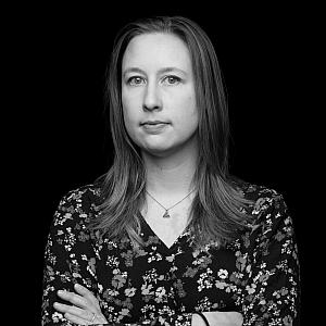 Portrait photo of a woman journalist, Ashley Luthern, standing with her arms crossed over a plain black background.