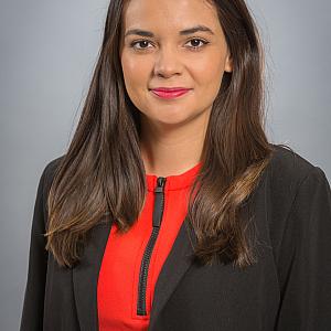 Person in red dress with black blazer and long brownish hair looking directly at the camera