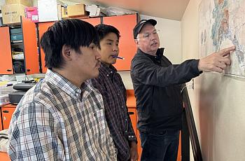 Person pointing to a map while speaking to 2 others