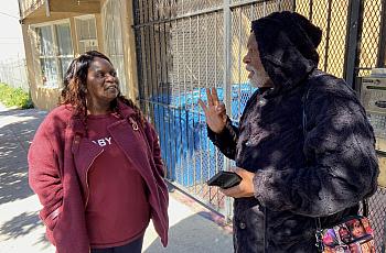 Two people talking, one wears a red top and another a black hoodie