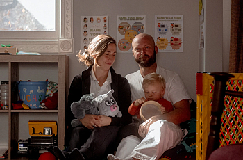 2 people sitting together, one with a child in their lap