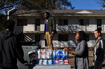 Residents place cases of water on a vehicle.