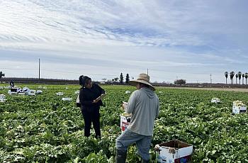 An organizer in a field and sunhat conducts outreach among farmworkers in California. 
