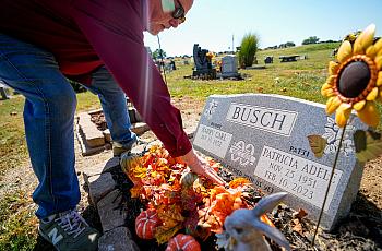 Person putting flowers on a toubstone