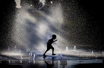 A young boy runs through a fountain.
