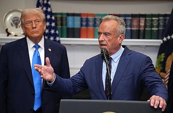 RFK Jr. stands before a podium, with President Trump behind him, at a White House press conference.