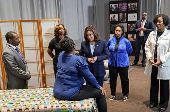 Person seated on a bed talking someone surrounded by people