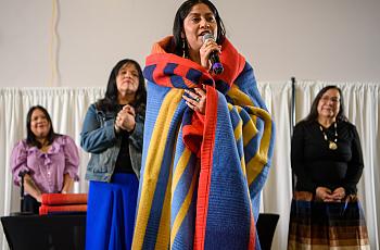 Huwighurruk Tribal Health Program graduate Desirae Barragan, wrapped in a colorful blanket, introduces herself in her native language during the Huwighurruk blanket ceremony in 2025. 