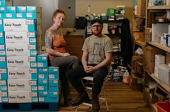 Two people sitting with a stack of needle boxes 