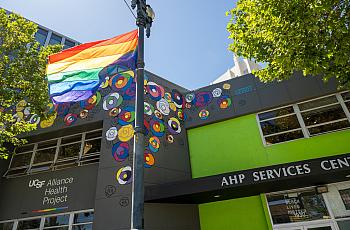 A rainbow flag flies in front of two buildings in San Francisco, including UCSF Alliance Health Project