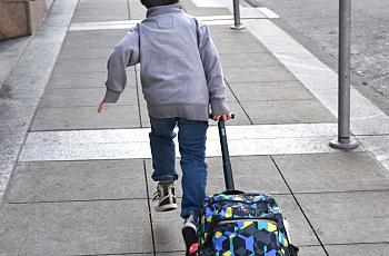Young person running on a pavement dragging a bag with wheels