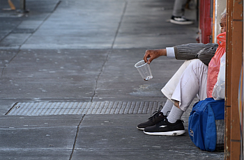 Person sitting on a sidewalk holding a cup 