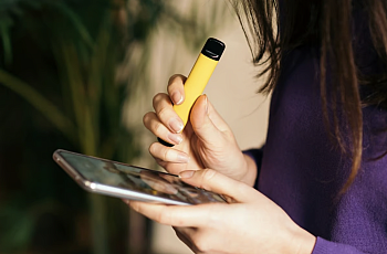 Person with yellow vape in one hand and phone in the other