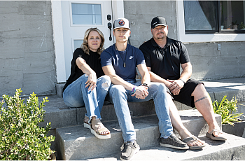 3 people seated on stairs in front of a door