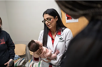 Person in a doctor's coat holding a baby