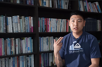 A young Korean man sits in a library making a gun gesture with his hand