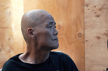 An older balding Korean man sits in profile inside a community shelter in Los Angeles