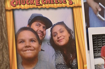 Alma Ramirez, her partner José, and their seven-year-old son smile inside a photobooth at Chuck E. Cheese’s. 