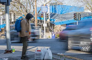 Person standing on a pavement with two plastic bags besides them
