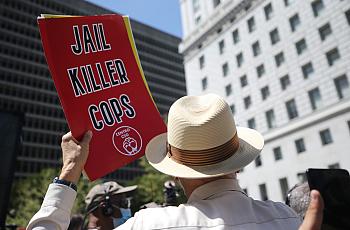 A person in hat holding banner saying "Jail Killer Cops"