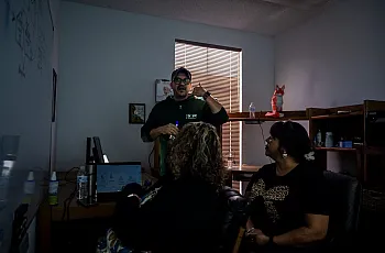 A man leads a discussion in a dimly lit office as two women listen.