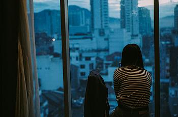 A woman stares out an apartment window.