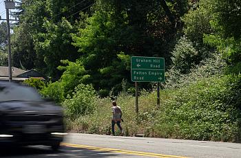 Car zooming through a road with greenery in the background and a person walking