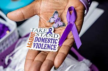 An image of a person's hand holding sticker which says "Take stand against Domestic Violence"