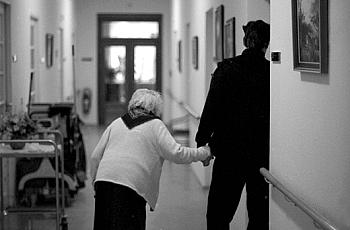 A person walking an old lady inside nursing home.