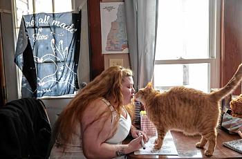 Woman leans toward orange cat on table.