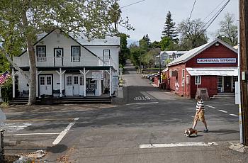Man walking a dog past a general store in a quiet small town.