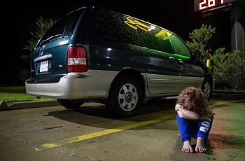 In a Victoria motel parking lot, Zoey Bowman sits on the ground and pouts in front of her mother's minivan in September.