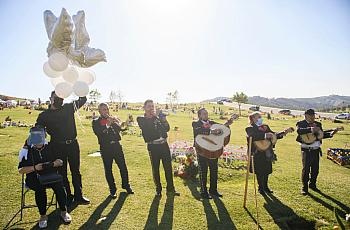 Rosa Mejia (L) listens as a mariachi band plays during a burial service for her husband Gilberto Arreguin Camacho, 58