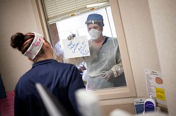 Nurses in the intensive care unit of MedStar St. Mary's Hospital communicate through a window with an erasable whiteboard from a
